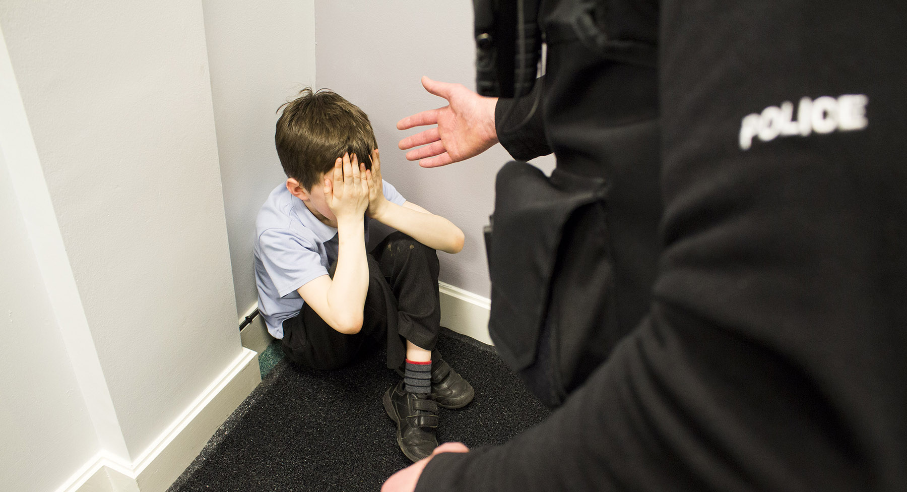 A boy sat crossed legged in the corner with a police with an outstretched arm